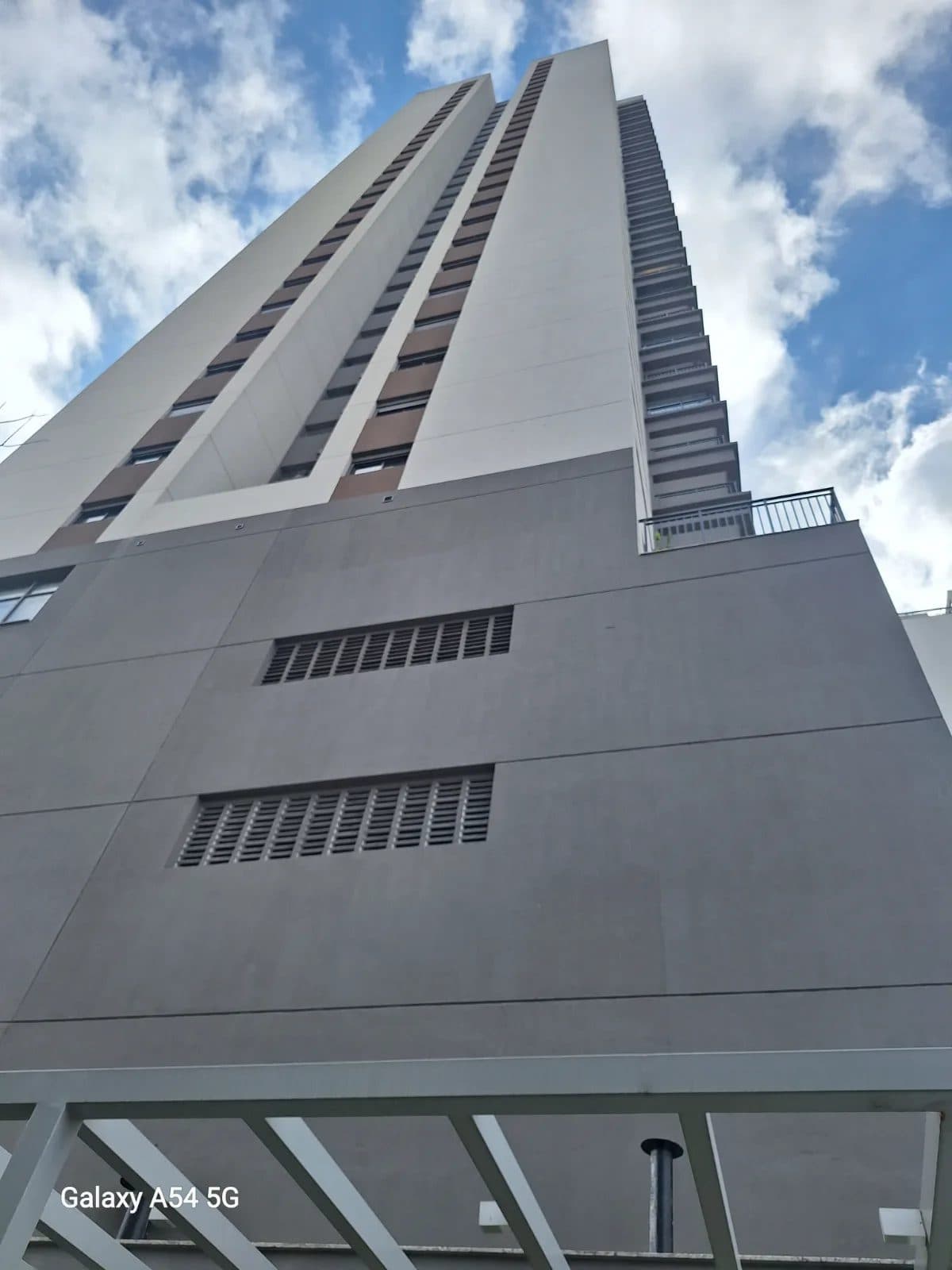 Fachada de prédio residencial moderno com tons de cinza e branco sob céu azul.